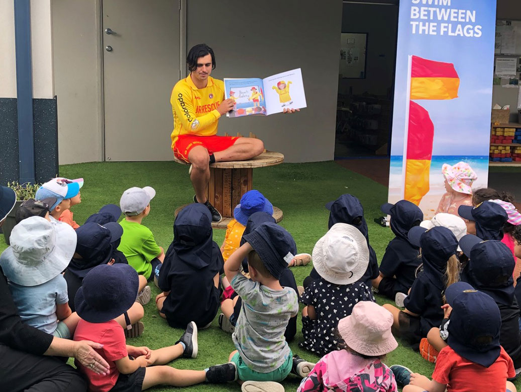 Surf lifesaver reading a book to young children
