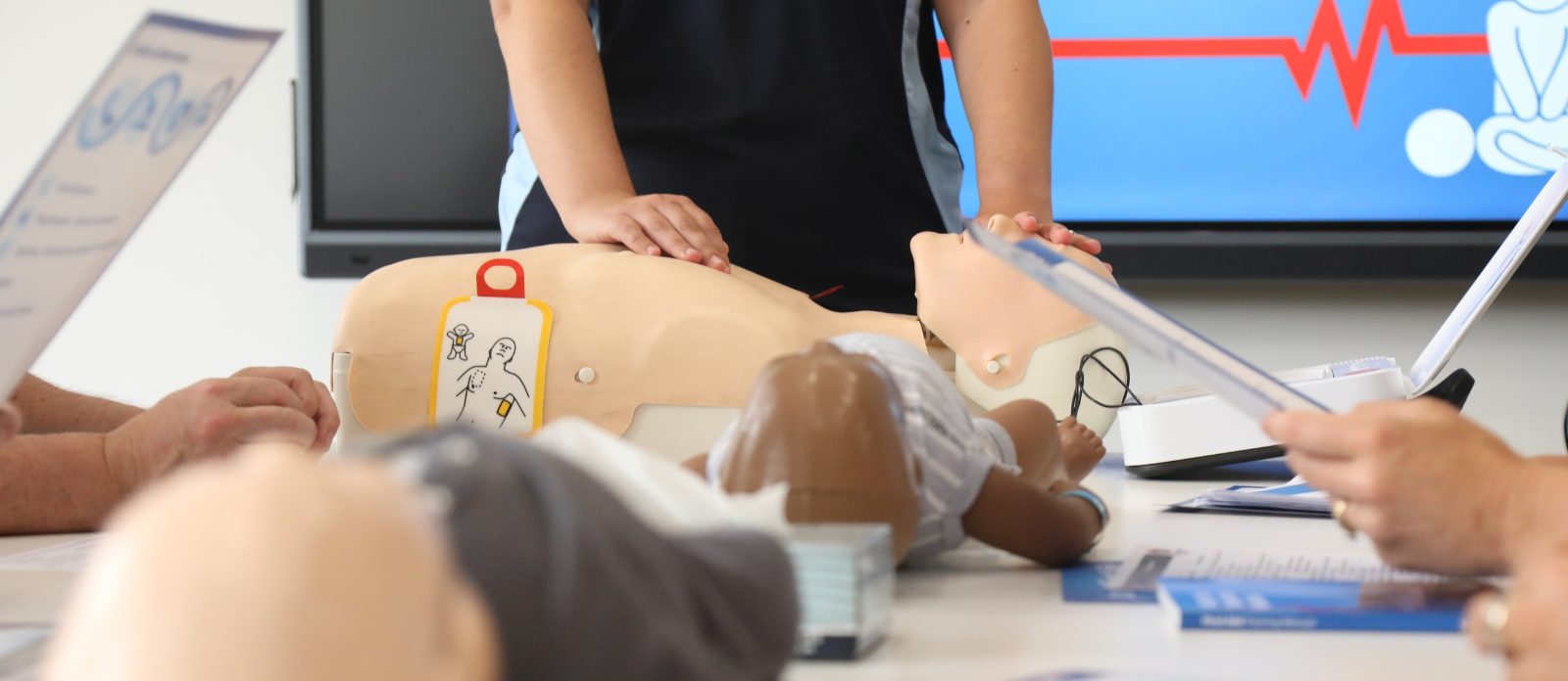 Training room showing a CPR dummy, and hands in the correct position about to administer an AED