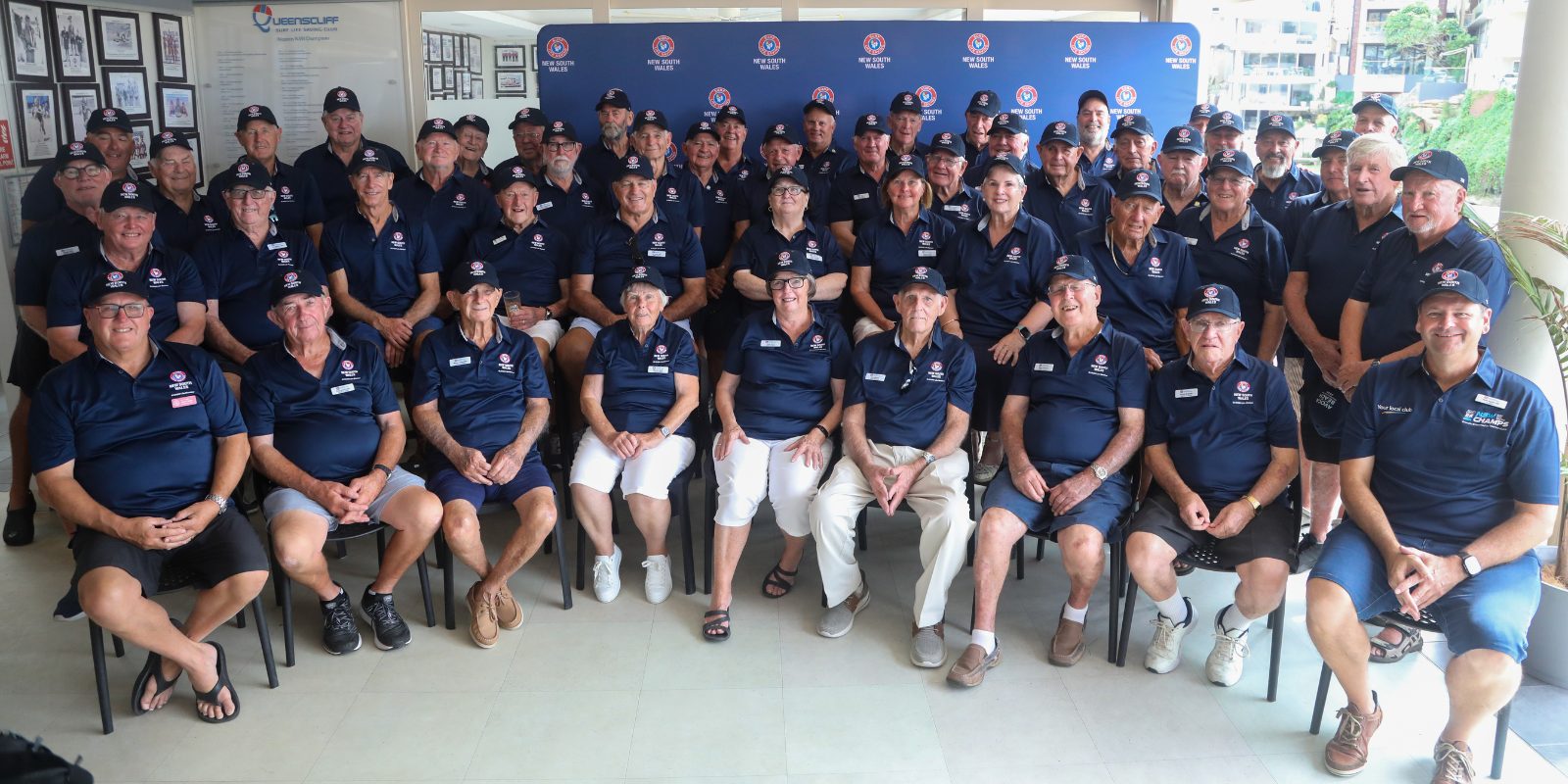 Group photo of Surf Life Saving NSW Life Members wearing navy uniforms and caps, seated and standing indoors.